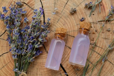Beautiful lavender flowers and bottles of essential oil on wooden stump, flat lay