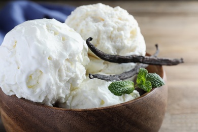 Photo of Yummy vanilla ice cream in wooden bowl, closeup