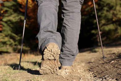 Hiker with trekking poles walking outdoors on sunny day, closeup