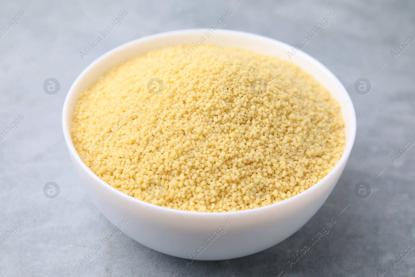 Photo of Raw couscous in bowl on gray table, closeup