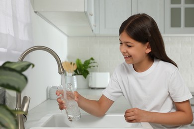 Photo of Girl filling glass with water from tap in kitchen