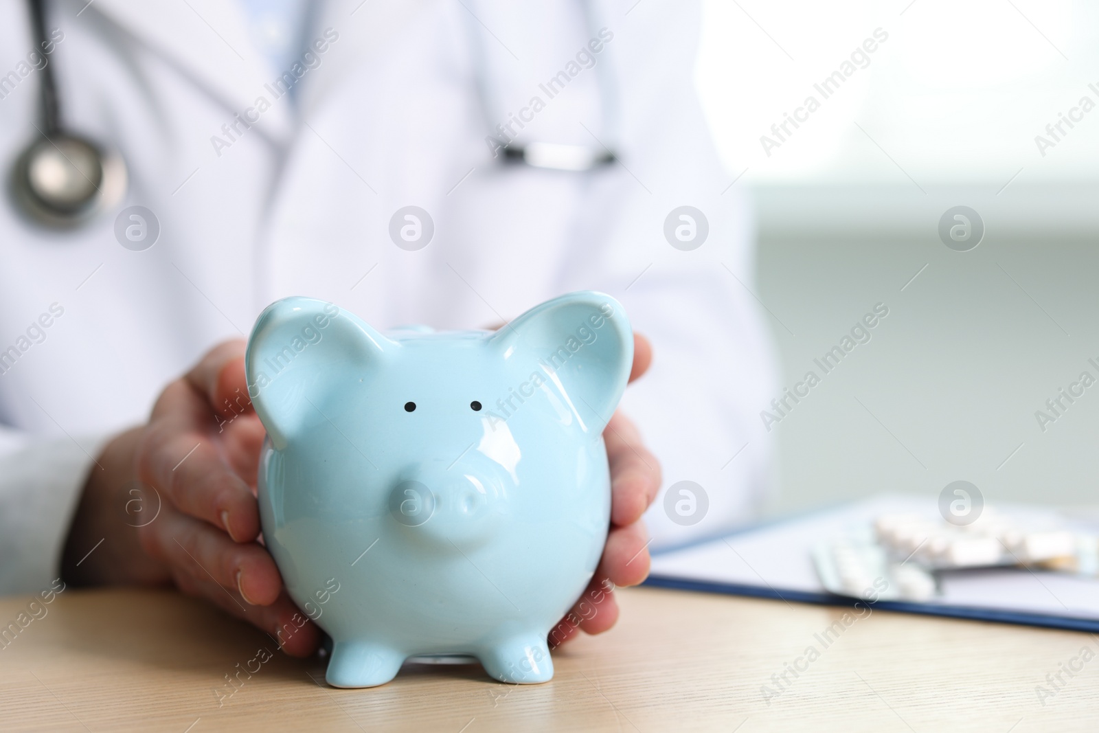 Photo of Doctor with piggy bank at wooden table, closeup