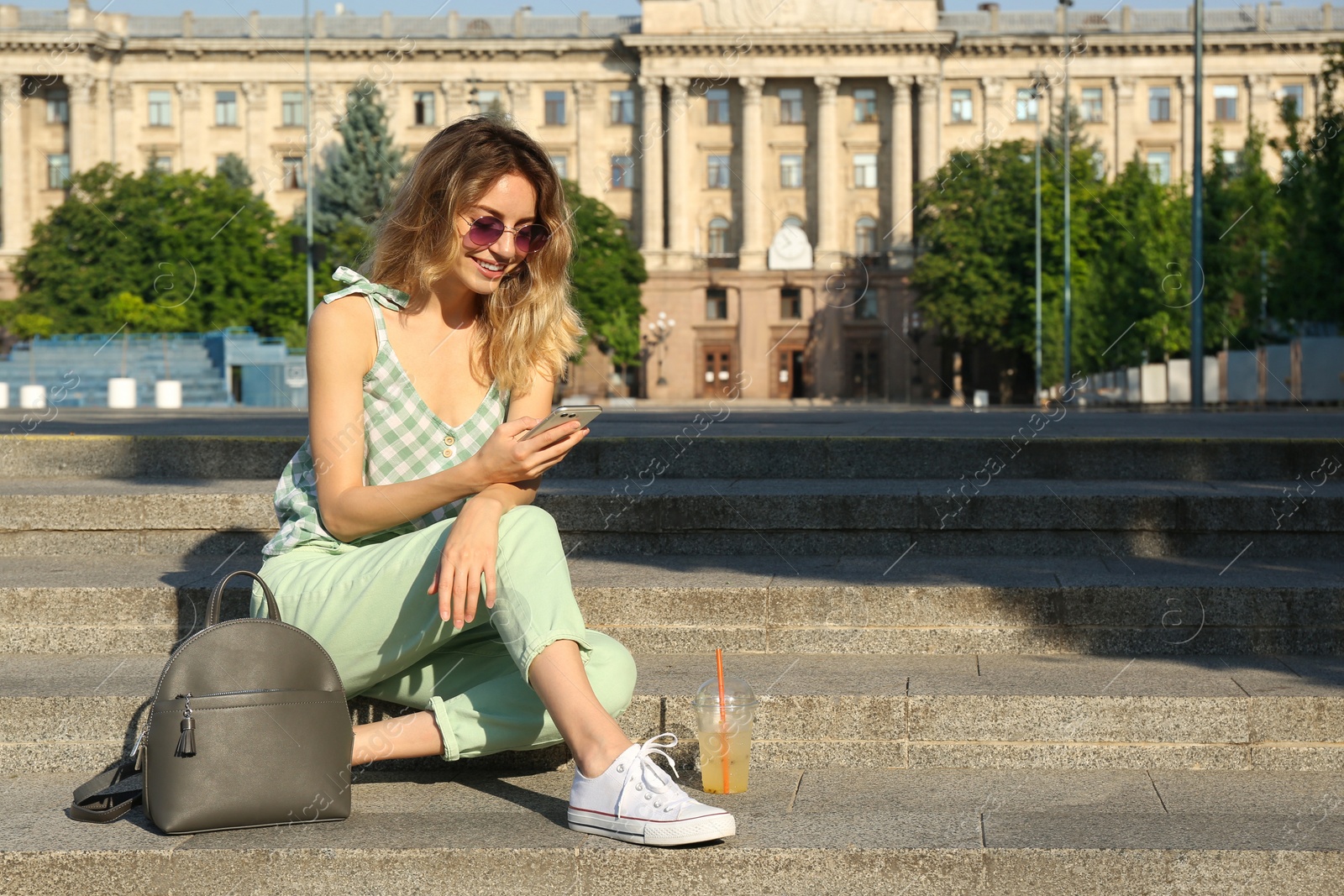 Photo of Young woman with stylish backpack and smartphone on stairs outdoors. Space for text