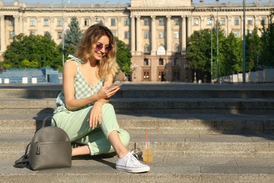 Photo of Young woman with stylish backpack and smartphone on stairs outdoors. Space for text