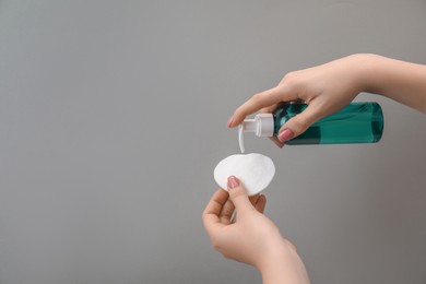 Photo of Woman applying makeup remover onto cotton pads on light grey background, closeup. Space for text