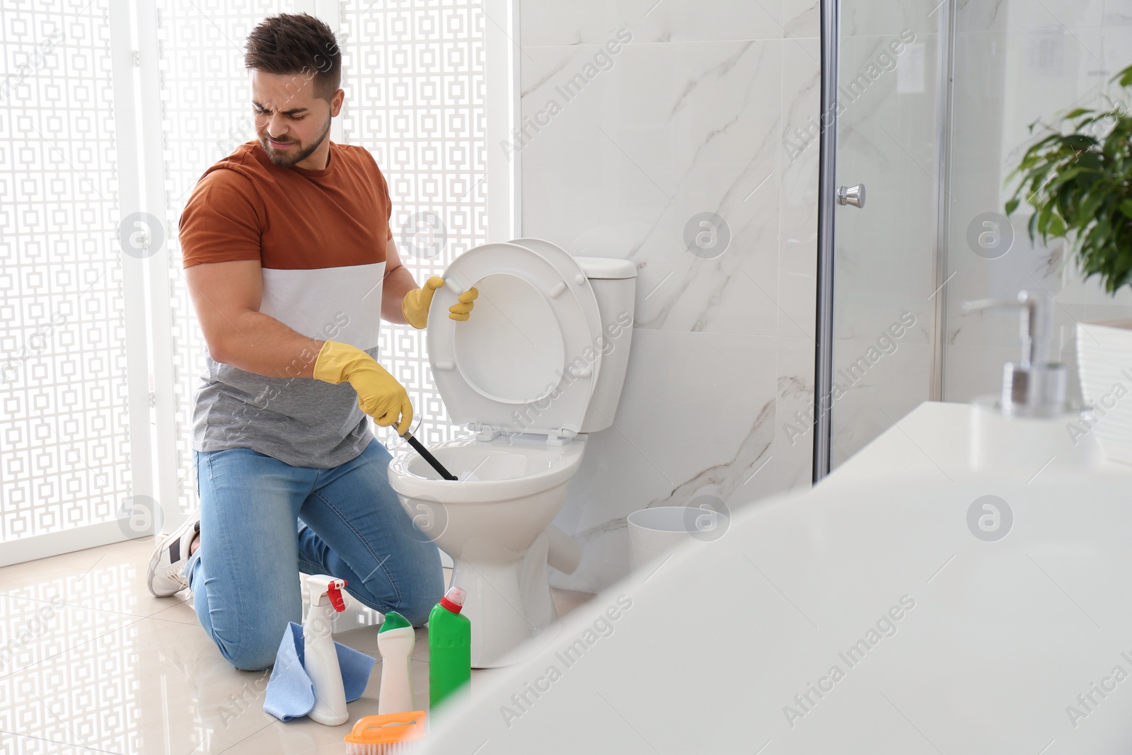 Photo of Young man feeling disgust while cleaning toilet bowl in bathroom