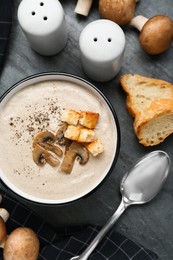 Photo of Delicious cream soup with mushrooms and croutons on black table, flat lay