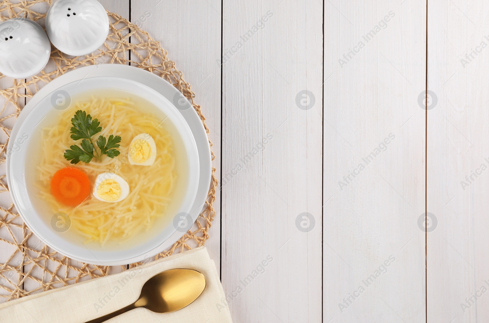 Photo of Tasty soup with noodles, egg, carrot and parsley in bowl served on white wooden table, flat lay. Space for text
