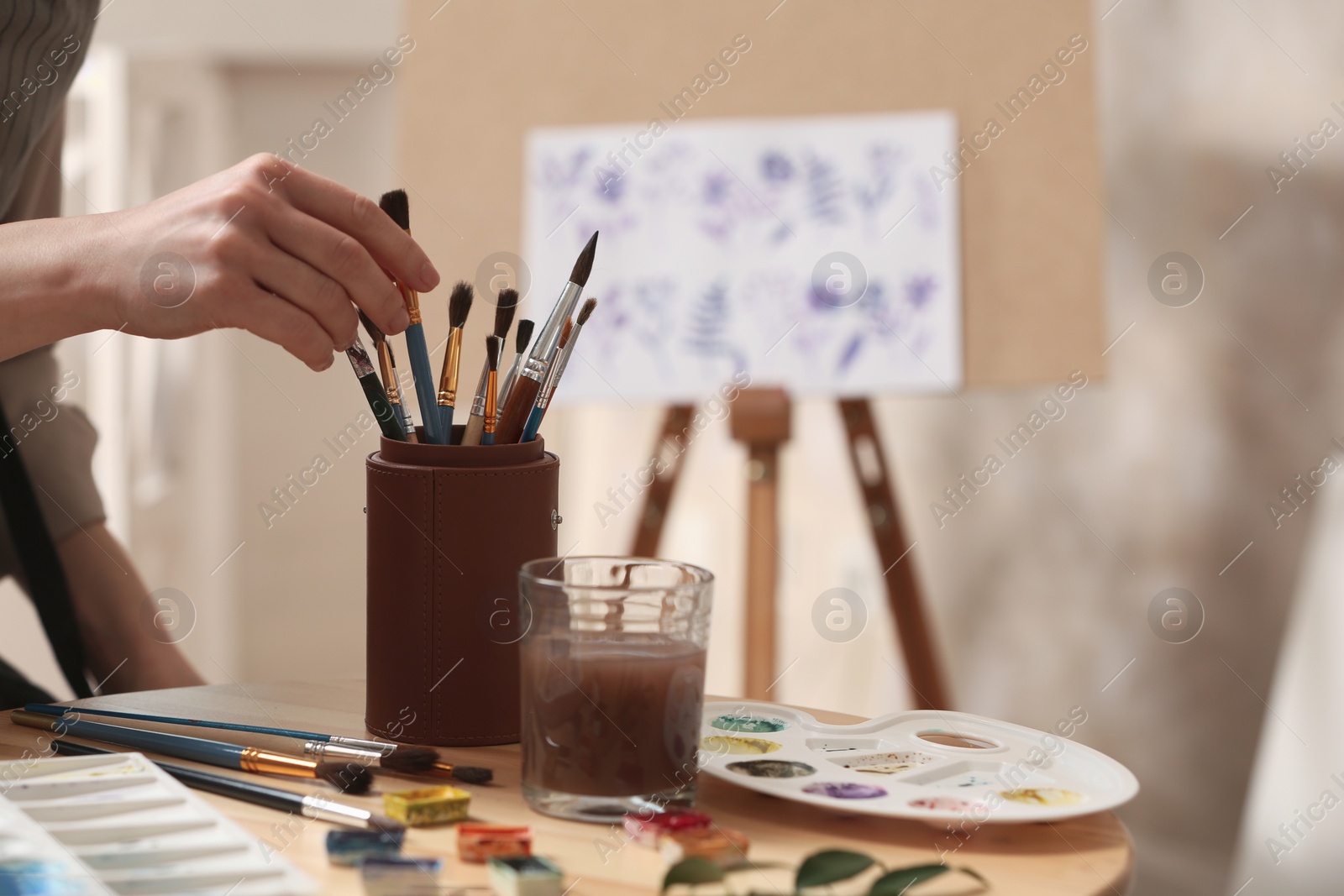 Photo of Watercolorist taking brush from holder on table in workshop, closeup
