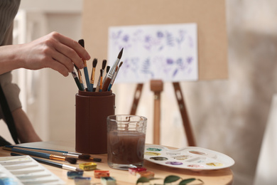 Watercolorist taking brush from holder on table in workshop, closeup