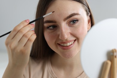 Photo of Smiling woman drawing freckles with brush indoors, closeup