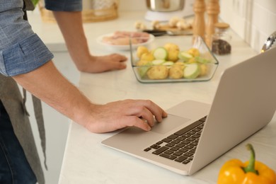 Man making dinner while watching online cooking course via laptop in kitchen, closeup