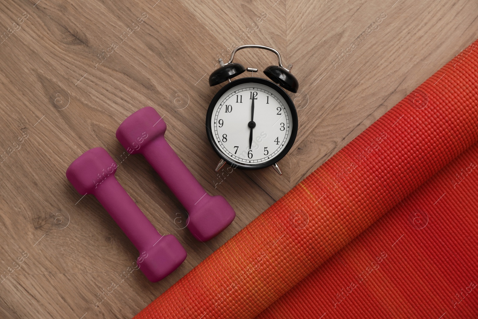 Photo of Alarm clock, yoga mat and dumbbells on wooden background, flat lay. Morning exercise