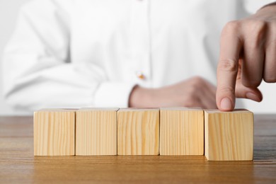 Photo of Woman arranging empty cubes in row on wooden table, closeup. Space for text