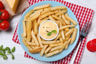 Delicious French fries and cheese sauce with basil served on white wooden table, flat lay