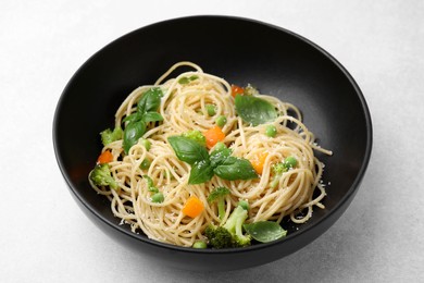 Delicious pasta primavera with basil, broccoli and peas on light grey table, closeup