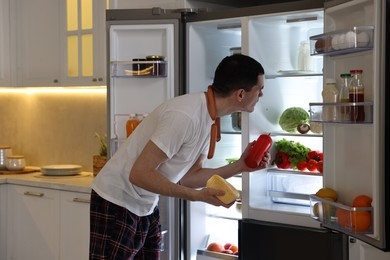 Photo of Man with ketchup, cheese and sausages near refrigerator in kitchen