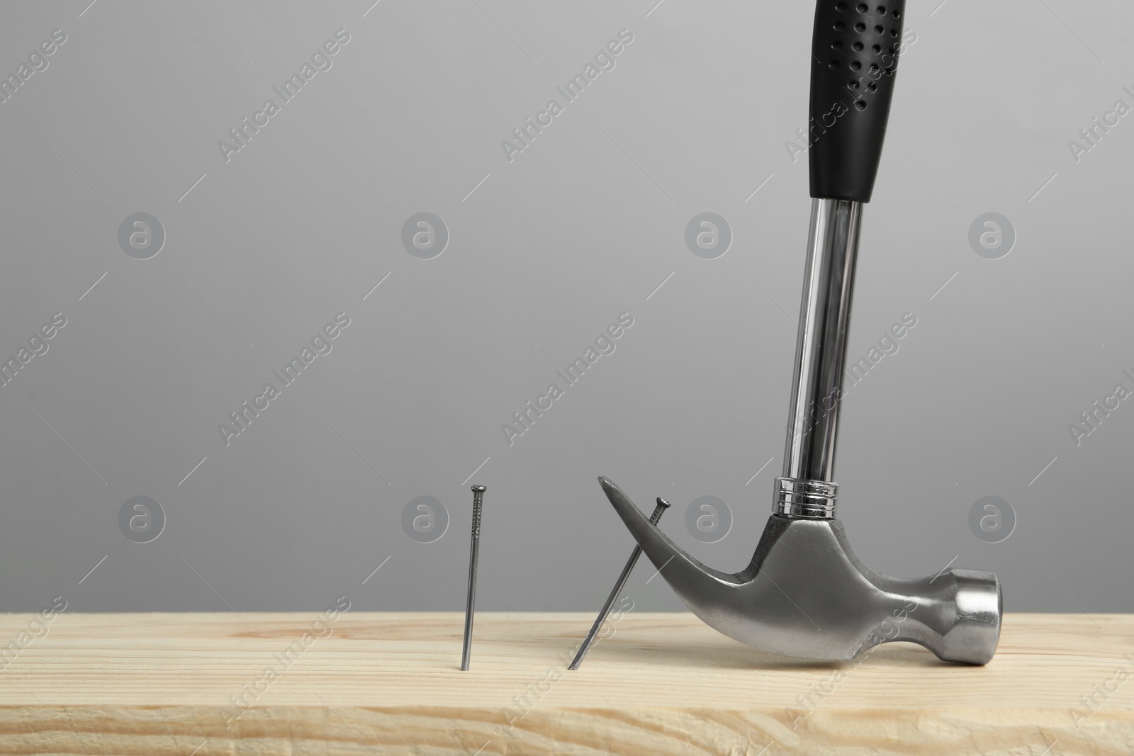 Photo of Hammer pulling metal nail out of wooden surface against grey background, space for text