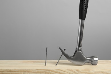 Photo of Hammer pulling metal nail out of wooden surface against grey background, space for text