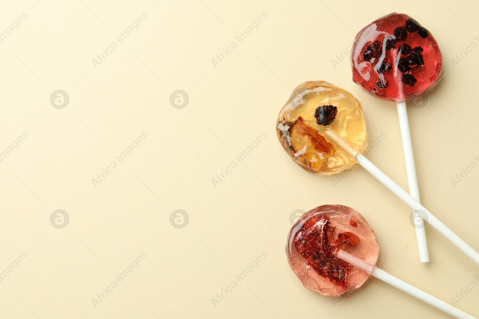 Photo of Sweet colorful lollipops with berries on beige background, flat lay. Space for text