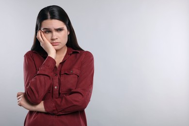 Sadness. Unhappy woman in red shirt on gray background, space for text
