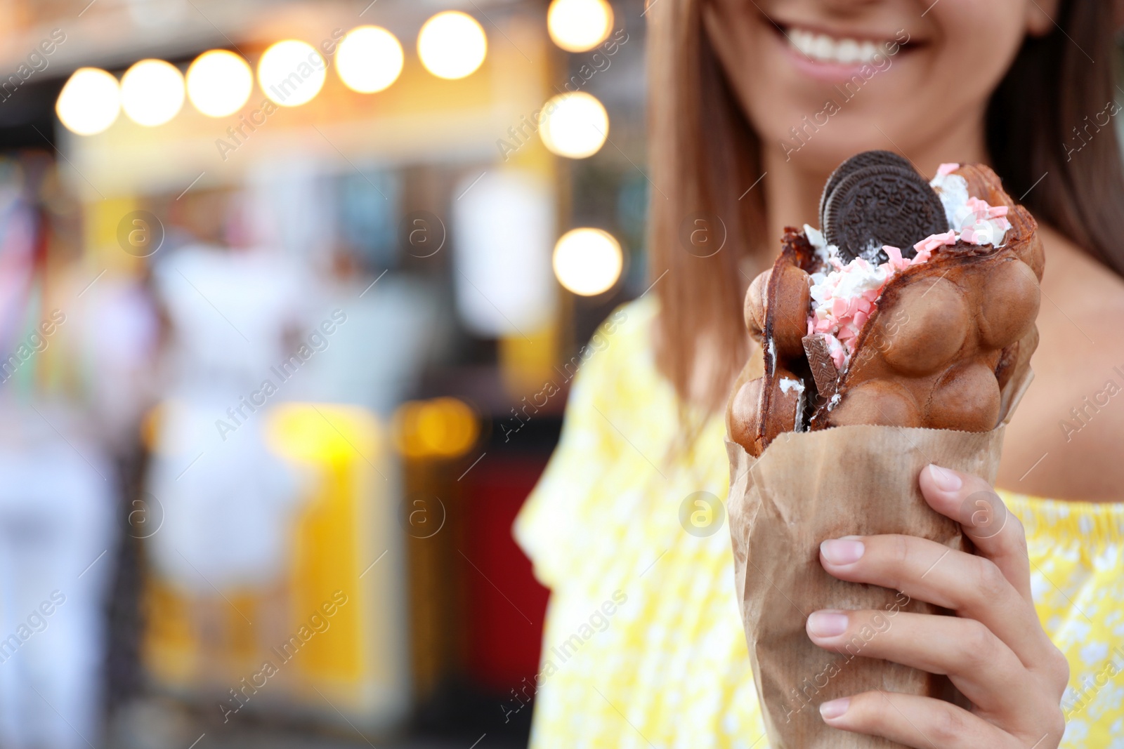 Photo of Young woman holding delicious sweet bubble waffle with ice cream outdoors, closeup