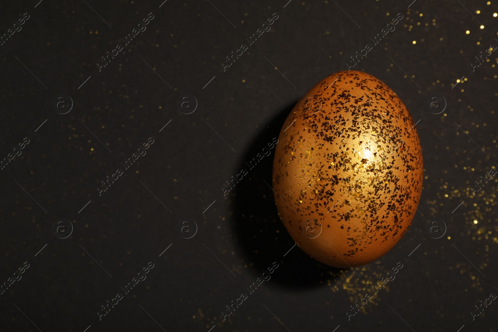 Photo of Shiny golden egg with glitter on black background, top view. Space for text