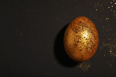 Photo of Shiny golden egg with glitter on black background, top view. Space for text