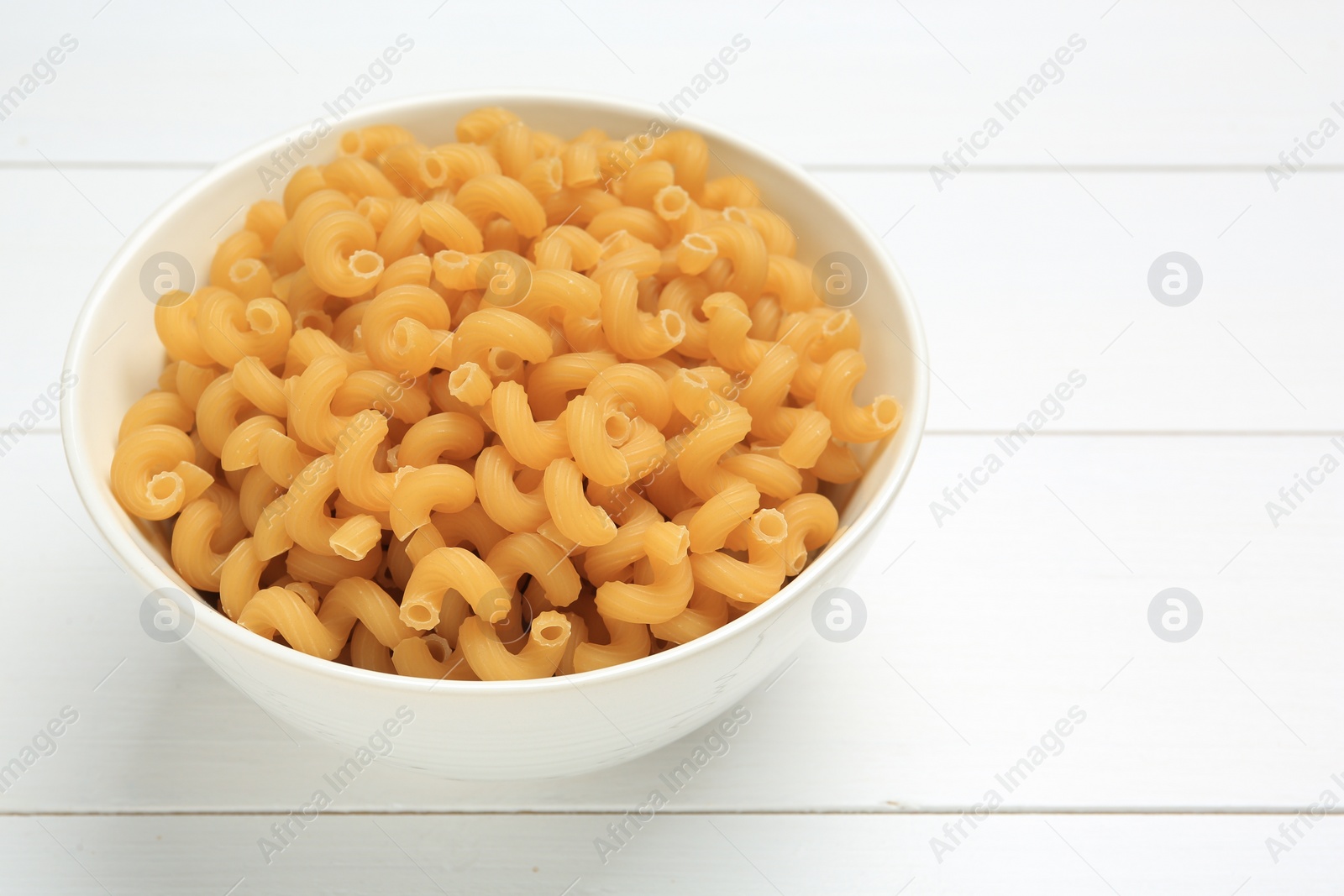 Photo of Raw cavatappi pasta in bowl on white wooden table, closeup. Space for text