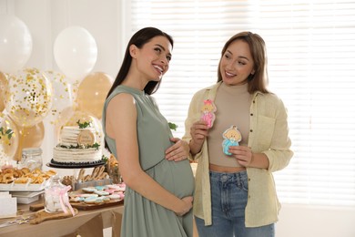 Photo of Happy pregnant woman and her friend with tasty cookies at baby shower party