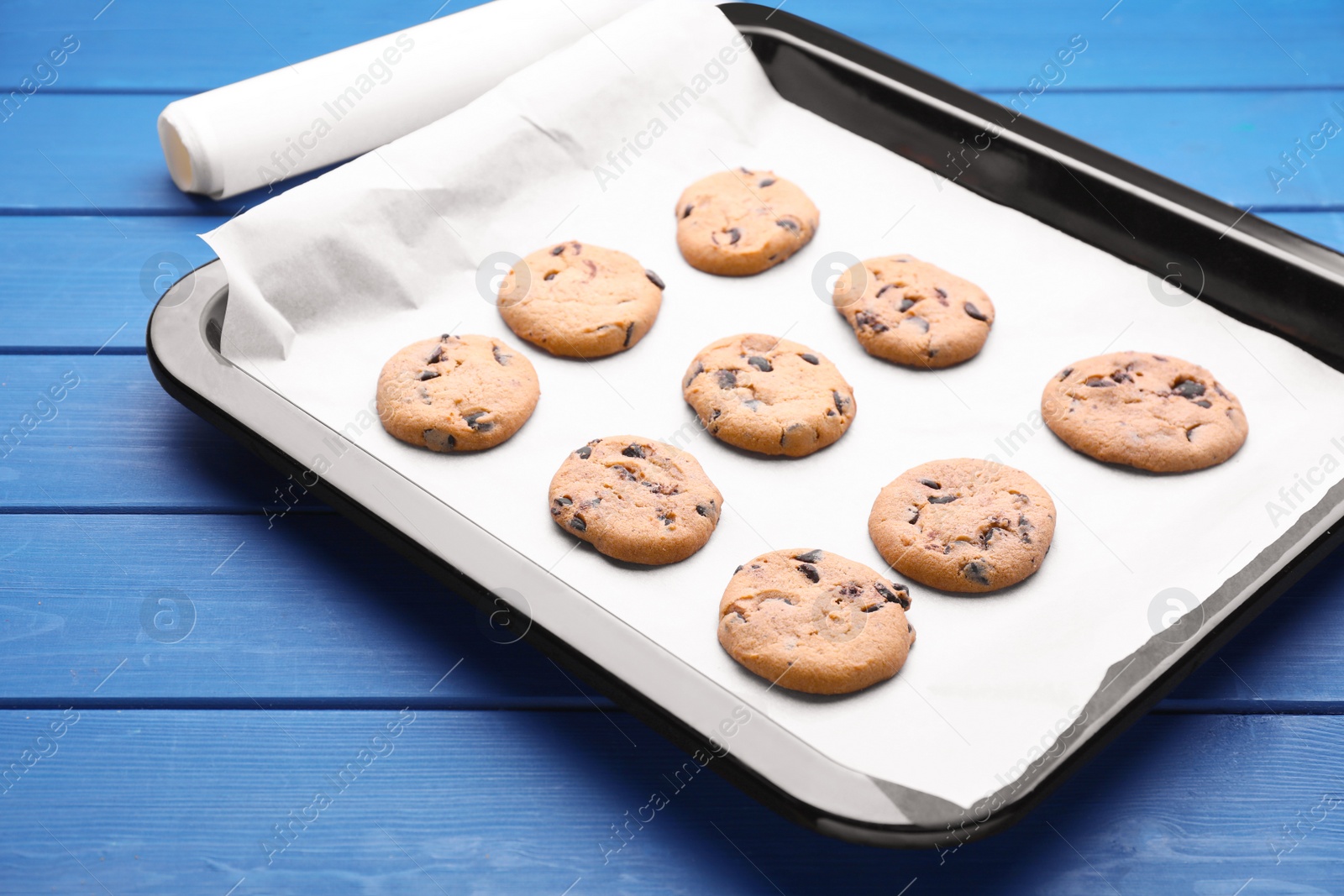 Photo of Baking pan with cookies and parchment paper on blue wooden table