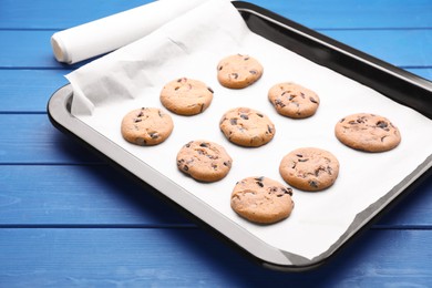 Baking pan with cookies and parchment paper on blue wooden table