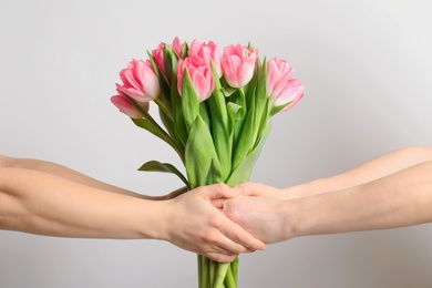 Photo of Man and lady holding bouquet of beautiful spring tulips on light background, closeup. International Women's Day