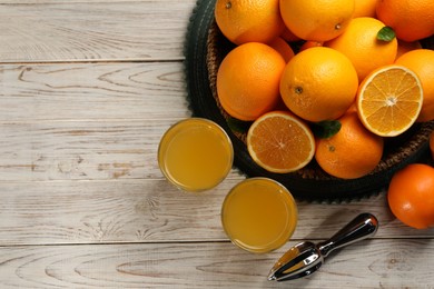 Photo of Many ripe juicy oranges, squeezer and fresh juice on white wooden table, flat lay. Space for text