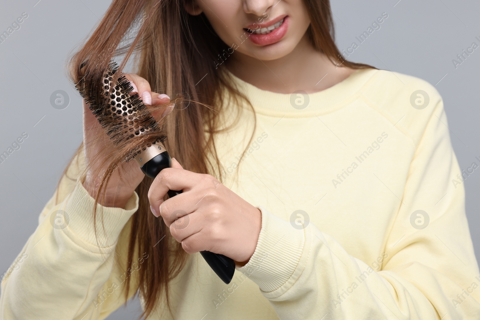 Photo of Woman brushing her hair on grey background, closeup. Alopecia problem