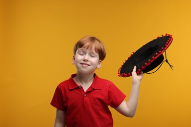 Cute boy with Mexican sombrero hat on yellow background