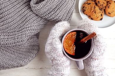 Woman with cup of hot mulled wine at white wooden table, top view. Winter drink