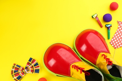 Photo of Flat lay composition with clown shoes and accessories on yellow background. Space for text