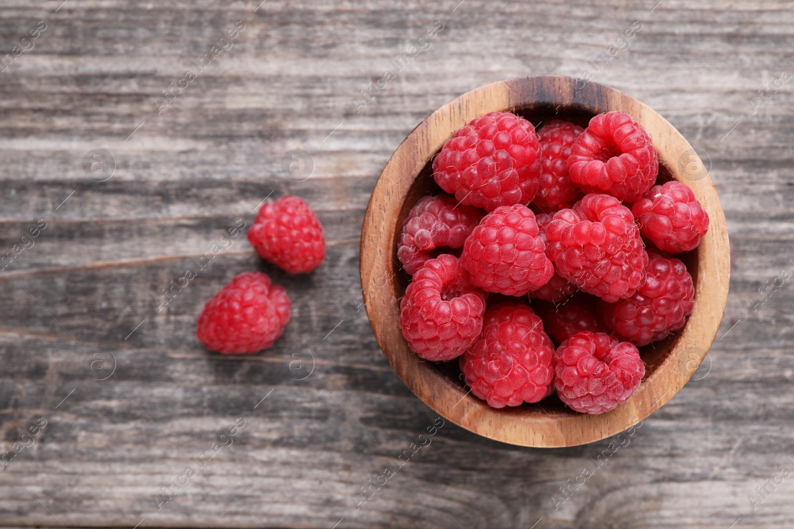 Photo of Tasty ripe raspberries in bowl on wooden table, top view. Space for text