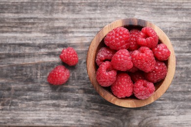 Photo of Tasty ripe raspberries in bowl on wooden table, top view. Space for text