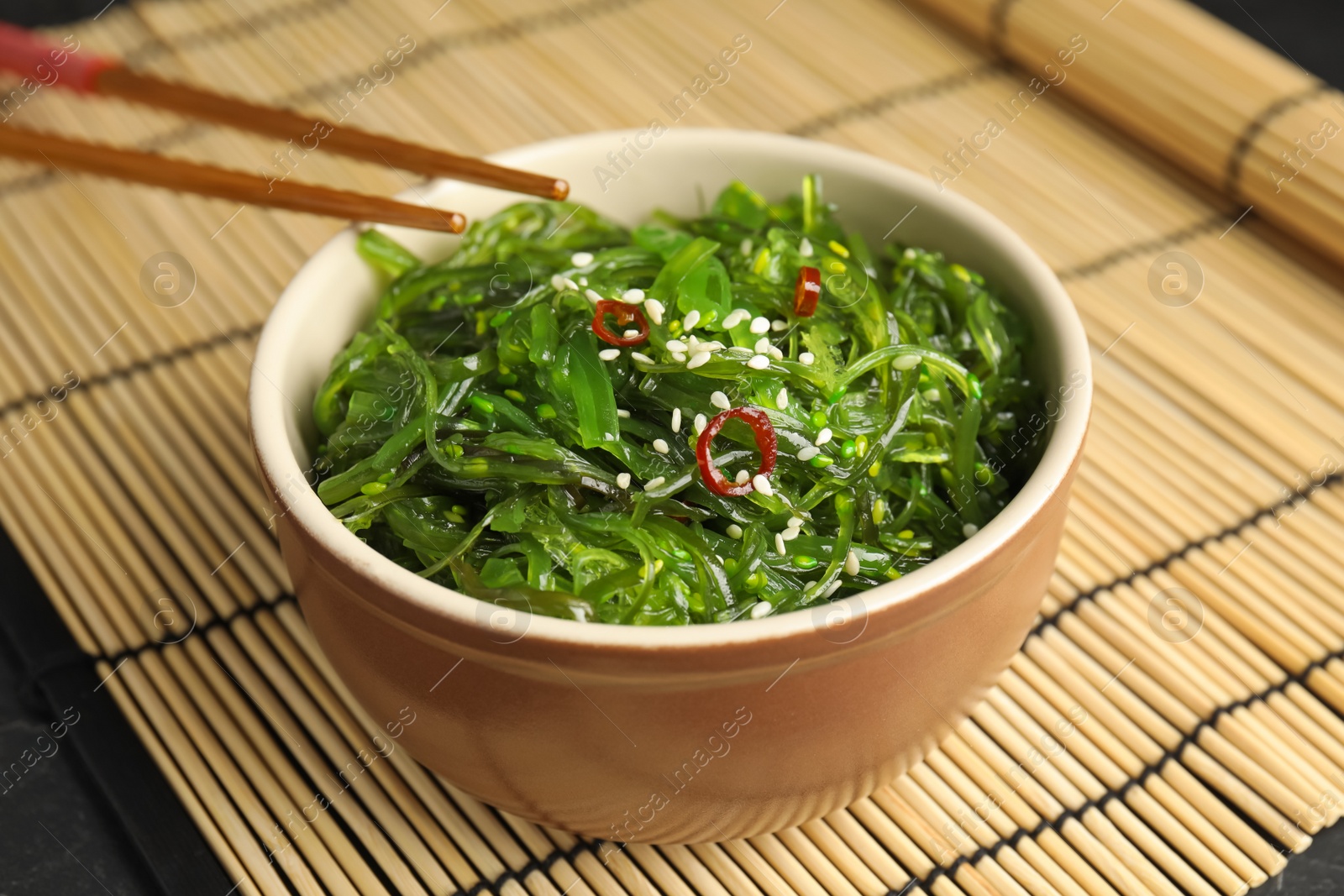 Photo of Chopsticks with Japanese seaweed salad in bowl on table, closeup