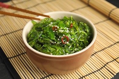 Chopsticks with Japanese seaweed salad in bowl on table, closeup