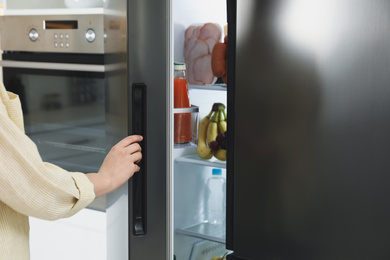 Photo of Young woman opening refrigerator indoors, closeup view