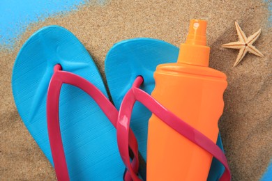 Photo of Flip flops, sunscreen and sand on light blue background, flat lay. Beach accessories