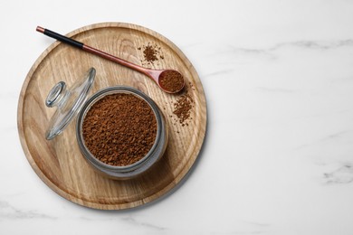 Photo of Jar of instant coffee and spoon on white marble table, top view. Space for text