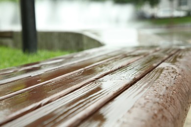 Wooden bench with water drops outdoors, closeup. Rainy weather