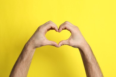 Photo of Man making heart with his hands on yellow background, closeup
