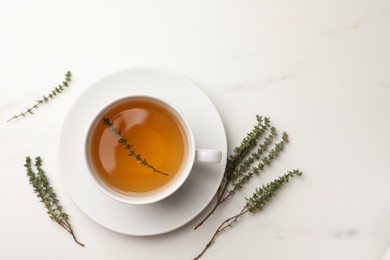 Cup of aromatic herbal tea with thyme on white marble table, flat lay. Space for text