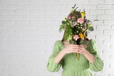 Woman covering her face with beautiful spring bouquet near white wall. Space for text