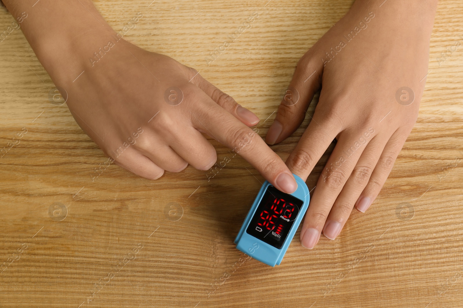 Photo of Man using pulse oximeter for oxygen level testing at wooden table, top view